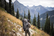 Hiker with a large backpack and walking poles ascending a mountain trail.